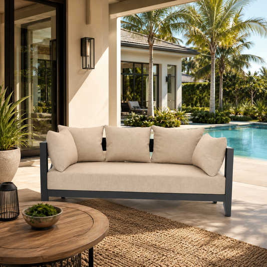 Beige outdoor sofa with cushions in a patio setting with palm trees and a pool.