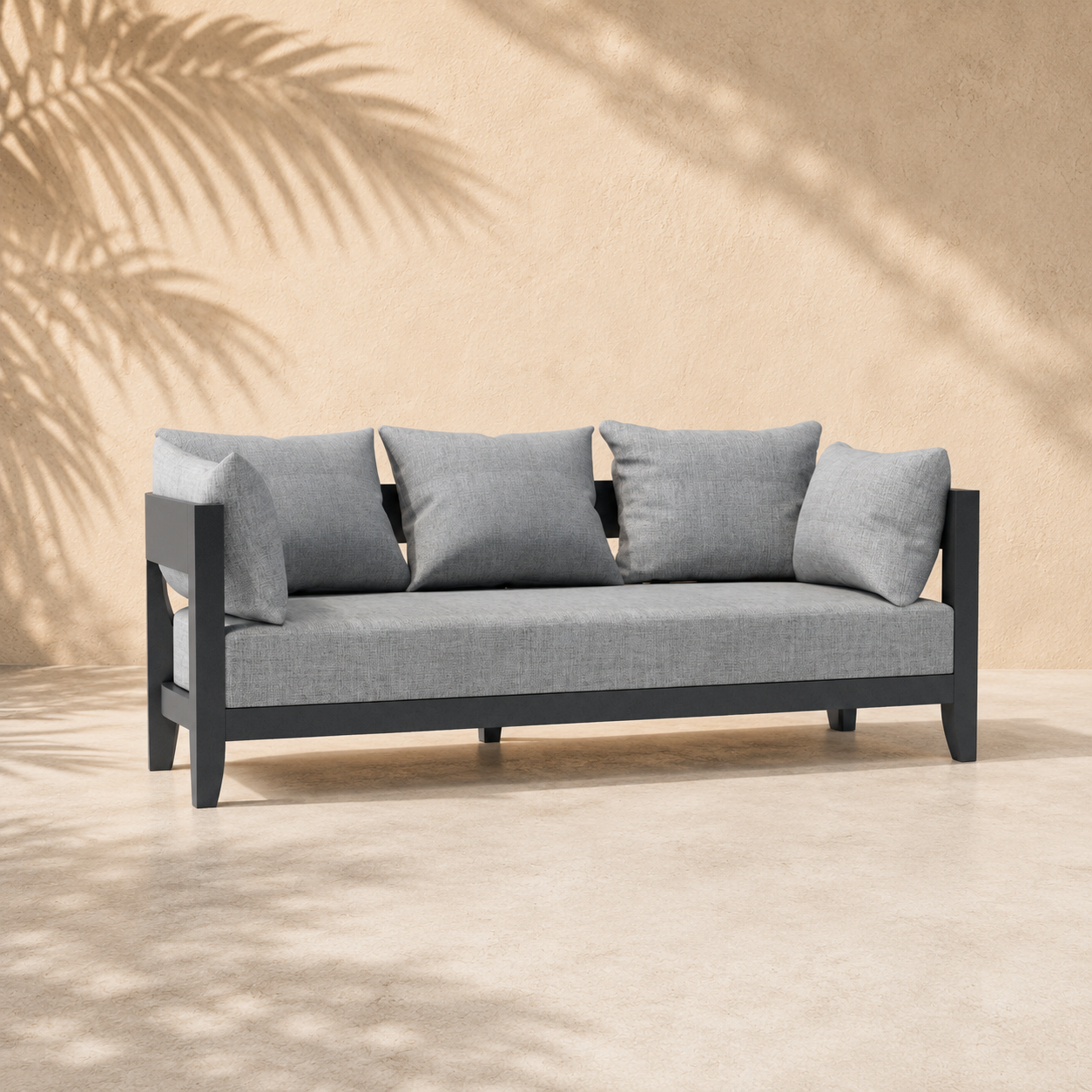 Gray sofa with cushions against a beige wall with palm leaf shadows