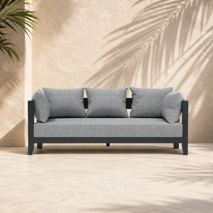 Gray sofa with black frame against a beige wall with plant shadows