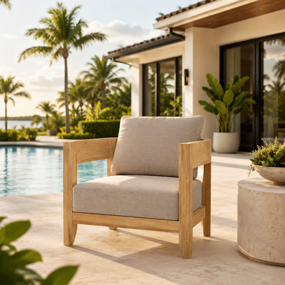 Wooden armchair with beige cushions on a patio by a poolside, with palm trees and a house in the background.