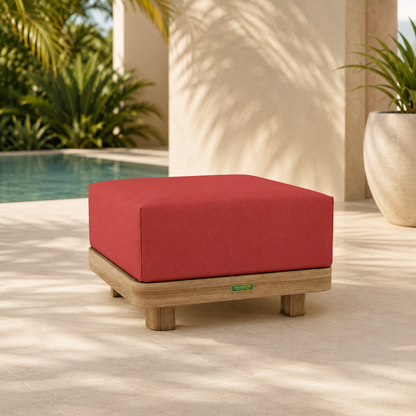Red cushioned ottoman on a patio with a pool and plants in the background